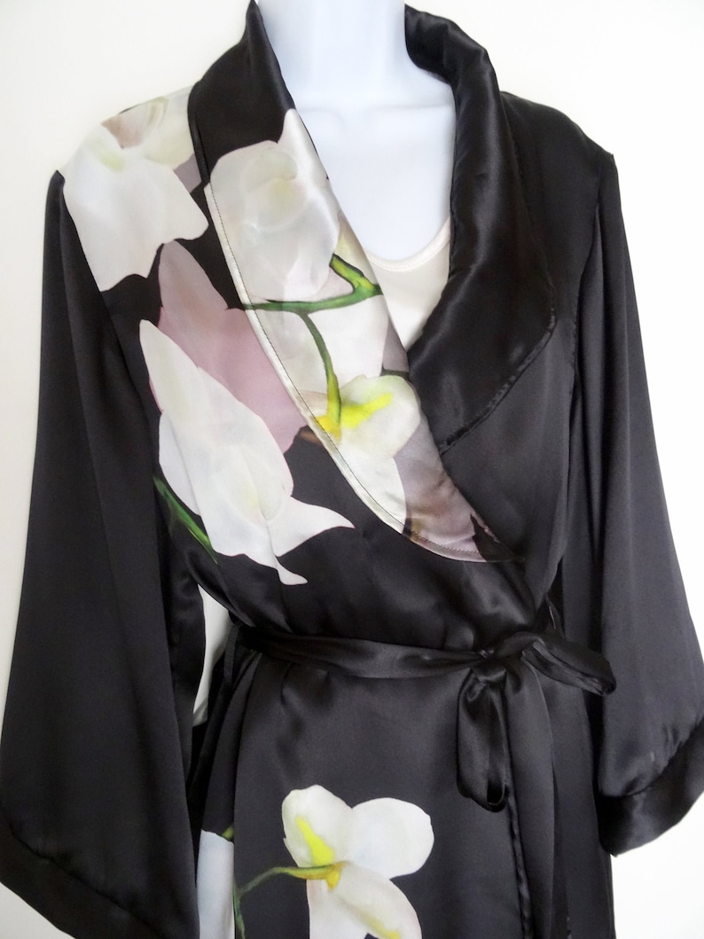May include: A black satin robe with a white floral print. The robe has a shawl collar and a tie belt.