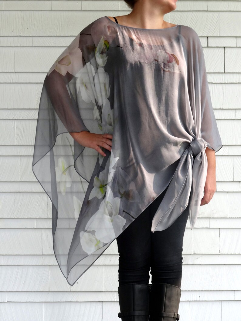 May include: A gray sheer top with white floral print. The top has a loose, flowing fit and is tied at the waist. The model is wearing black pants and boots.