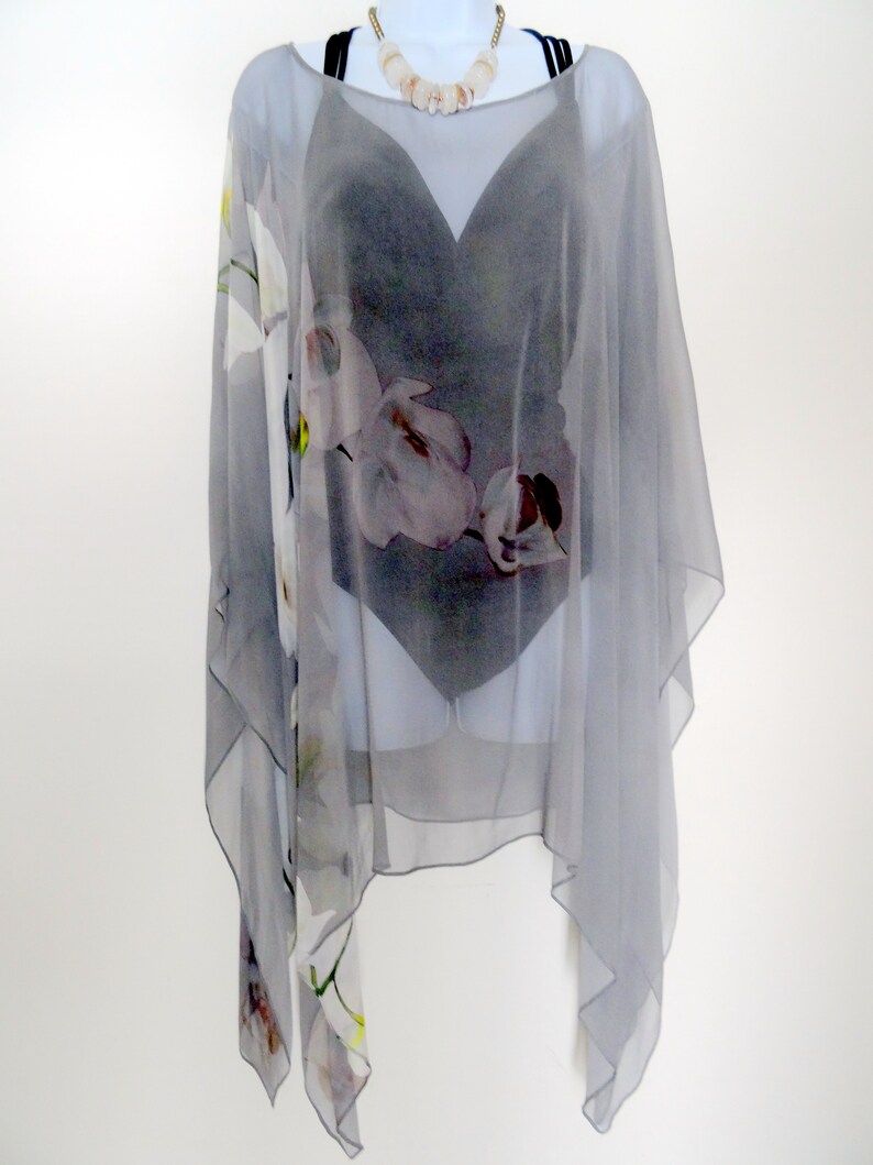 May include: A gray sheer poncho with a floral print. The poncho has a scoop neck and a loose fit.