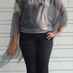 May include: A gray sheer top with a floral print and a long, flowing design. The top is worn with black jeans.