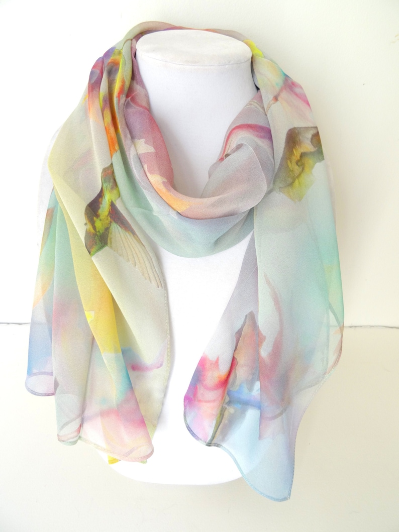 May include: A light blue silk scarf with a watercolor print of hummingbirds and flowers. The scarf is draped over a white mannequin.