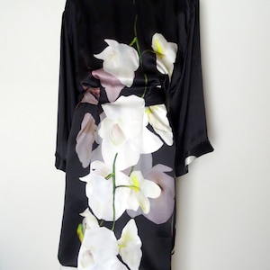 May include: A black silk robe with a white orchid floral print. The robe has long sleeves and a tie belt.