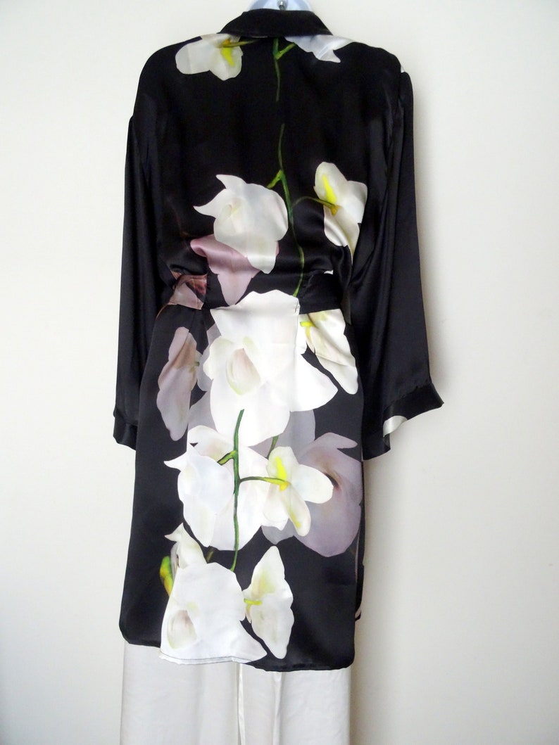 May include: A black silk robe with a white orchid floral print. The robe has long sleeves and a tie belt.