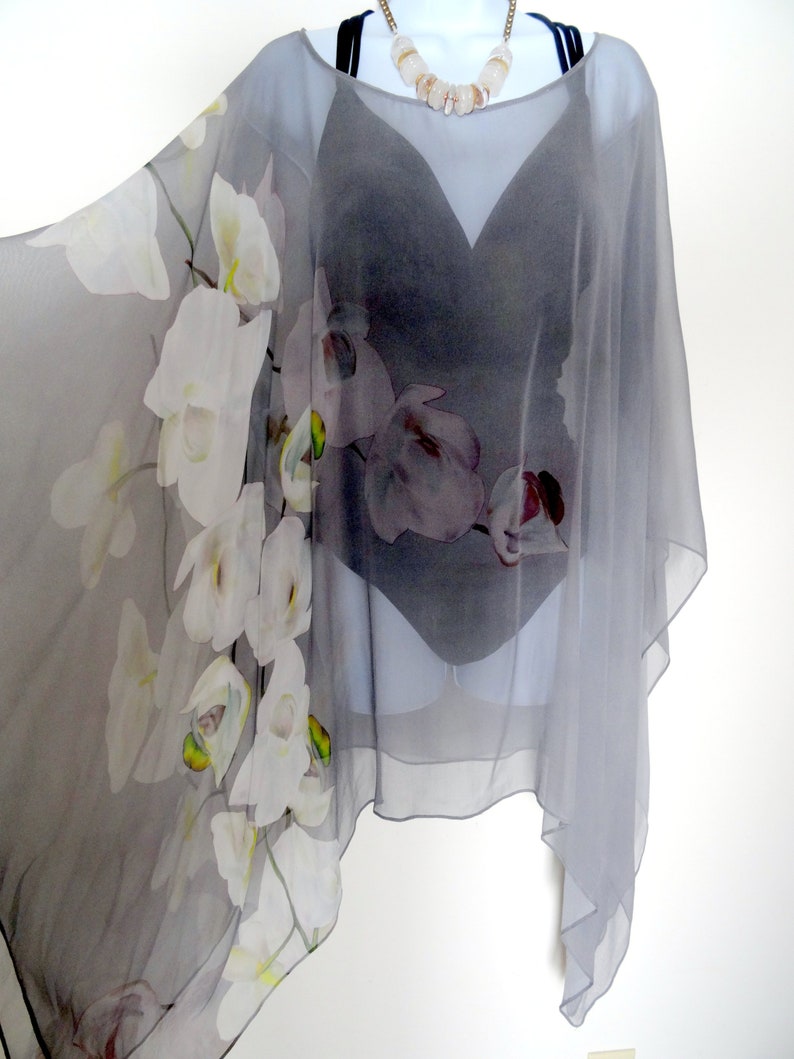 May include: A gray sheer poncho with a white orchid print. The poncho has a wide neckline and a loose fit.