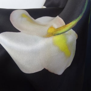 May include: Close-up of a black fabric with a white flower print. The flower has a yellow centre and a green stem.