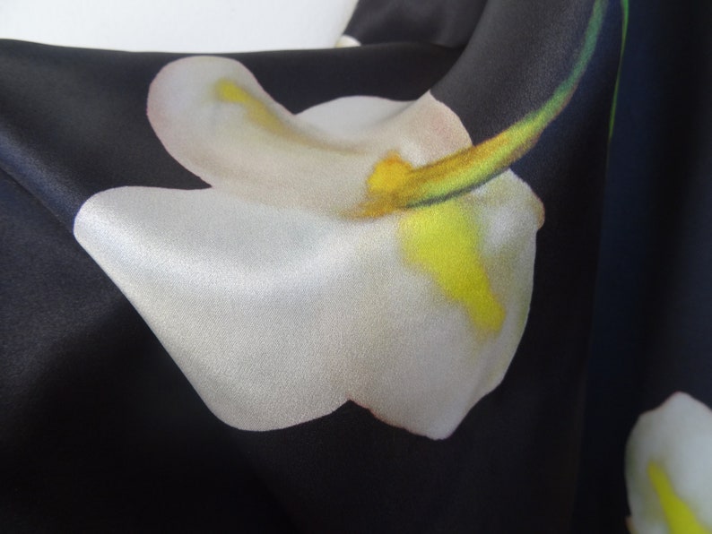 May include: Close-up of a black fabric with a white flower print. The flower has a yellow centre and a green stem.