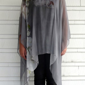 May include: A gray sheer top with a floral print. The top has a loose, flowing fit and a high neckline. The floral print is white and features a variety of flowers.