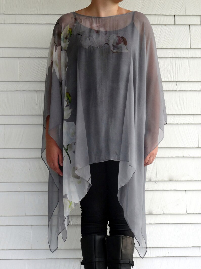 May include: A gray sheer top with a floral print. The top has a loose, flowing fit and a high neckline. The floral print is white and features a variety of flowers.
