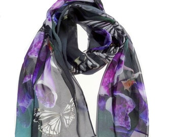 May include: A lightweight, semi-sheer scarf featuring a vibrant print of purple and blue floral shapes interspersed with detailed black and white butterfly illustrations against a dark, translucent background with flowing, draped fabric edges.