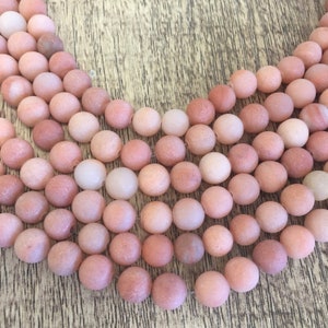 May include: A strand of pink and white agate beads. The beads are round and have a matte finish.