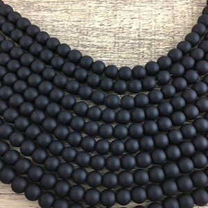 May include: A strand of black matte round beads. The beads are arranged in a circular pattern, creating a layered effect.