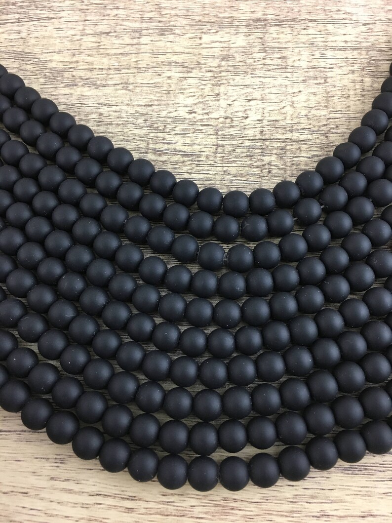 May include: A strand of black matte round beads. The beads are arranged in a circular pattern, creating a layered effect.