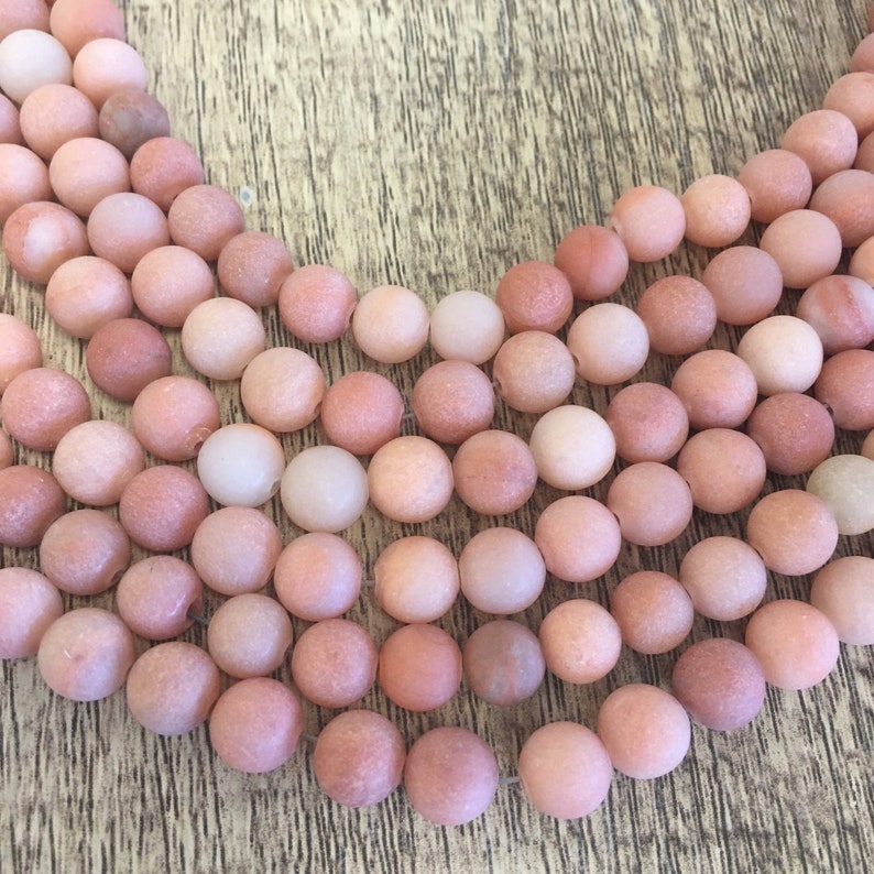 May include: A strand of pink and white agate beads. The beads are round and have a matte finish.