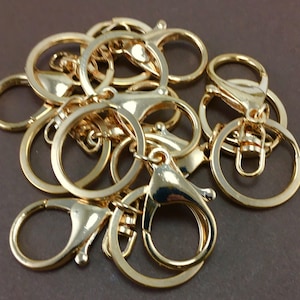 May include: A group of gold-colored key rings and key chain clips. The key rings are round and the key chain clips have a hook and a loop.