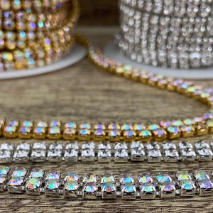 K&ouml;nnte beinhalten: Zwei Reihen von schimmernden Strass-Kettenbesatz, eine goldene und eine silberne, auf einer Holzoberfl&auml;che.