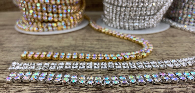 K&ouml;nnte beinhalten: Zwei Reihen von schimmernden Strass-Kettenbesatz, eine goldene und eine silberne, auf einer Holzoberfl&auml;che.