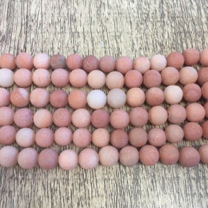 May include: A strand of round, pink and white agate beads. The beads have a matte finish and a slightly rough texture.