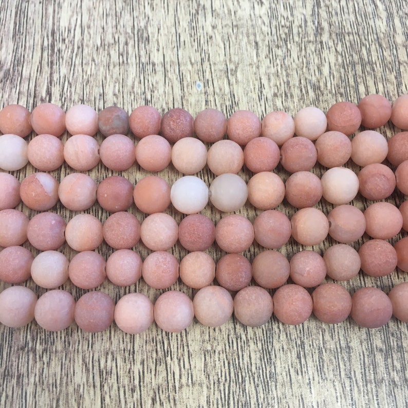 May include: A strand of round, pink and white agate beads. The beads have a matte finish and a slightly rough texture.