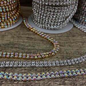 K&ouml;nnte beinhalten: Drei Spulen mit Strassbesatz, eine gold, eine silber und eine schillernd. Der Besatz ist zweireihig und hat quadratische Strasssteine.