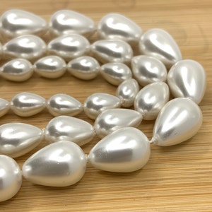 May include: A strand of white pearlescent teardrop-shaped beads. The beads are arranged in a circular pattern, with the largest beads in the centre and the smallest beads on the outside.