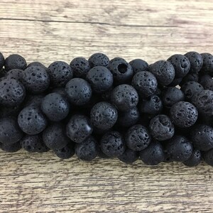 May include: A close-up of a strand of black lava rock beads. The beads are round and have a rough, textured surface.
