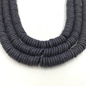May include: Close-up of three strands of dark gray, flat, round beads. The beads have a textured surface and are strung together, creating a layered effect. The background is plain white, highlighting the beads' color and texture.