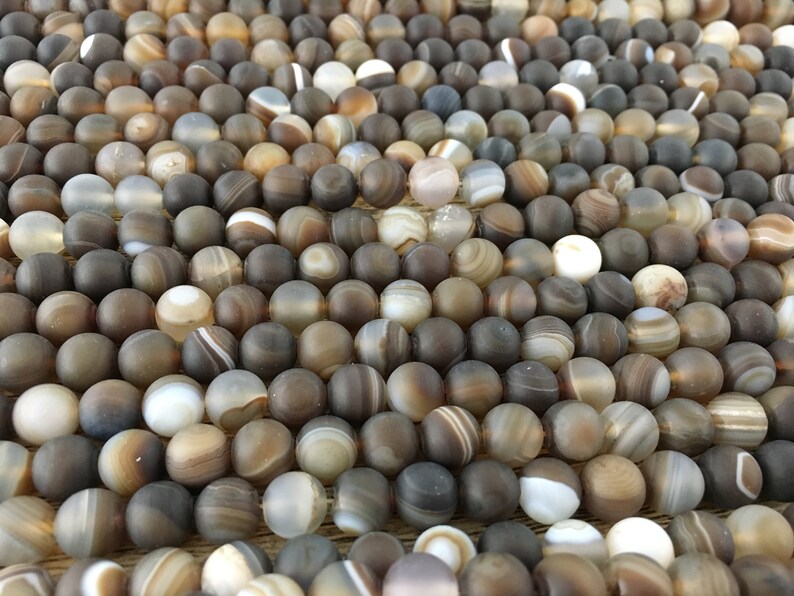 May include: A close-up of a collection of round, brown agate beads with white and gray banding. The beads are smooth and polished, and they have a natural, earthy look.