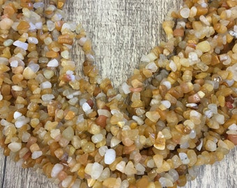 May include: A close-up view of a collection of small, irregularly shaped, polished gemstones. The stones are primarily shades of yellow, orange, and white, with a mix of opaque and translucent pieces. The gemstones are likely used for jewelry making or crafts.
