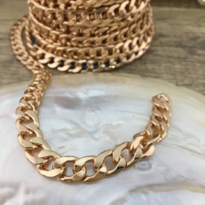May include: A gold-toned curb chain necklace with a thick, flat link design. The chain is displayed on a white, pearlescent surface.