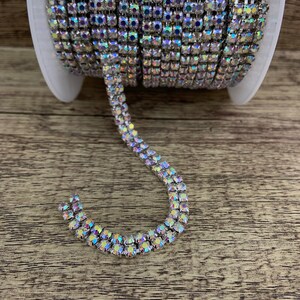 K&ouml;nnte beinhalten: Eine Rolle silberne Strass-Kettenborte mit schillernden Steinen. Die Kette ist auf einer Spule und ein Abschnitt der Kette ist S-f&ouml;rmig drapiert.