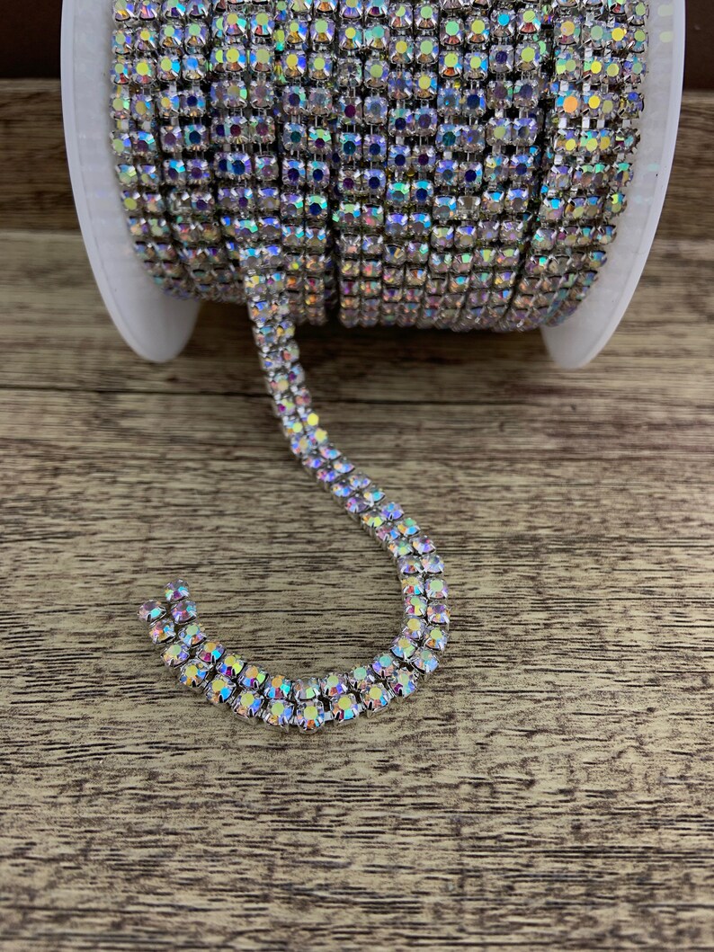 K&ouml;nnte beinhalten: Eine Rolle silberne Strass-Kettenborte mit schillernden Steinen. Die Kette ist auf einer Spule und ein Abschnitt der Kette ist S-f&ouml;rmig drapiert.