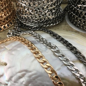 May include: Three curb chains in gold, silver, and black metal. The chains are laid out on a white, iridescent surface.