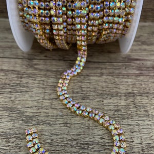 K&ouml;nnte beinhalten: Eine Rolle goldfarbener Strass-Kettenbesatz mit schillernden Steinen. Die Kette ist zweireihig und hat einen zarten, funkelnden Look.