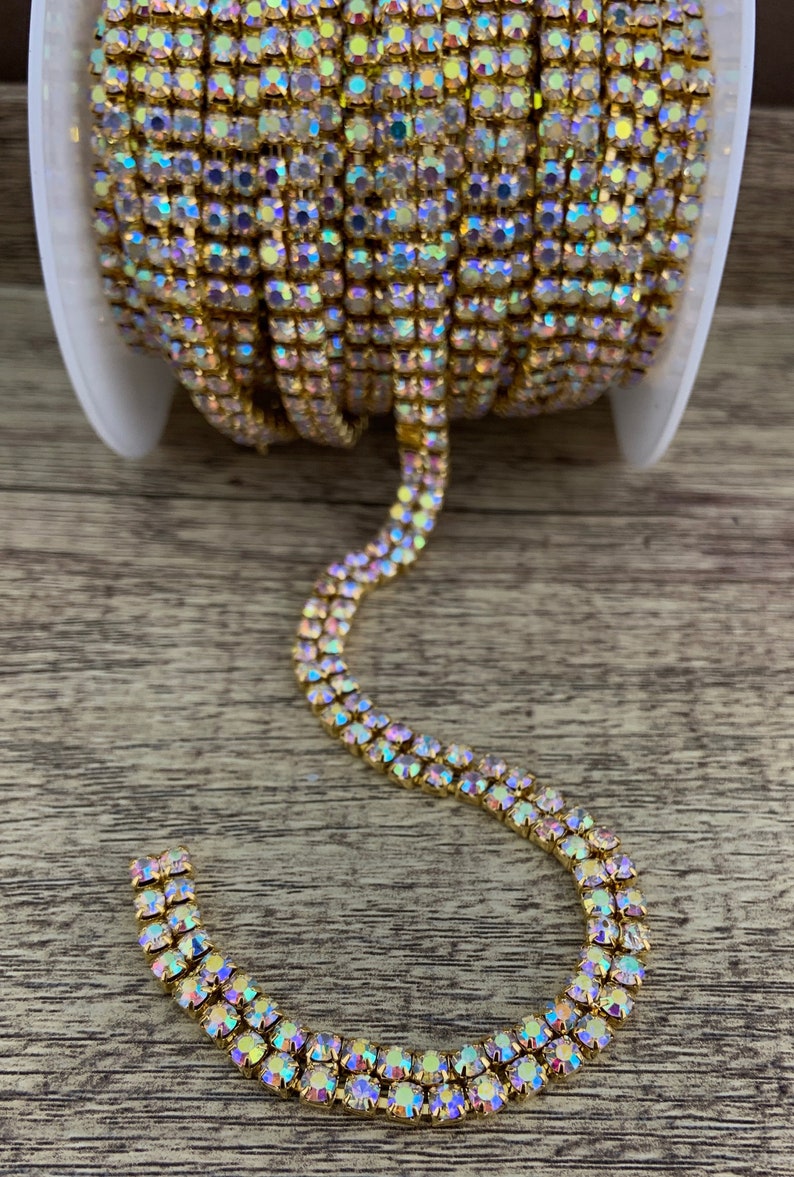 K&ouml;nnte beinhalten: Eine Rolle goldfarbener Strass-Kettenbesatz mit schillernden Steinen. Die Kette ist zweireihig und hat einen zarten, funkelnden Look.