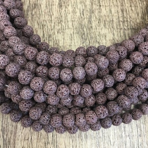 May include: A strand of dark purple lava rock beads. The beads are round and have a rough, textured surface.
