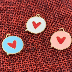 May include: Three enamel charms in the shape of speech bubbles, each with a red heart. One is light blue, one is white, and one is pink. All have gold-colored edges and a small loop at the top for attaching to jewelry.