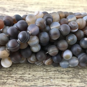 May include: A strand of round, gray agate beads with brown and white banding. The beads are smooth and polished.