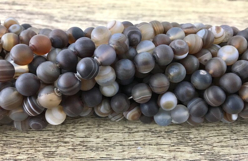 May include: A strand of round, gray agate beads with brown and white banding. The beads are smooth and polished.
