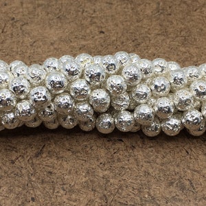 May include: A strand of silver lava rock beads. The beads are round and have a rough, textured surface.
