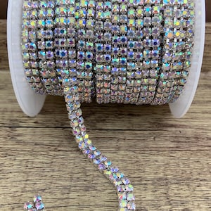 K&ouml;nnte beinhalten: Eine Spule mit silberner Strass-Kettenborte. Die Kette besteht aus kleinen, quadratischen Strasssteinen, die in einer silbernen Metallfassung gefasst sind. Die Kette ist schillernd und hat einen Regenbogeneffekt.