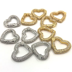 May include: A collection of heart-shaped charms. Some are silver-colored and encrusted with small, clear stones. Others are gold-colored and similarly adorned. The charms are designed with a clasp mechanism.