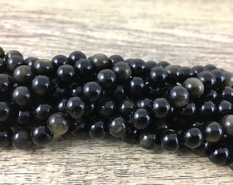 May include: A strand of black gemstone beads with a golden sheen. The beads are round and smooth, and they are arranged in a pile.