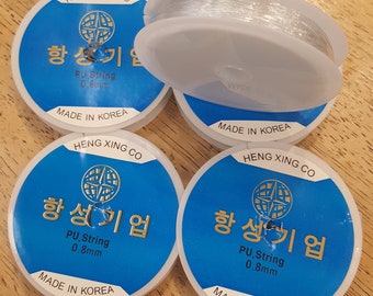 May include: Four spools of clear PU string, 0.8mm thick, are displayed. Each spool is on a blue and white label with Korean text and the words "HENG XING CO" and "MADE IN KOREA". One spool is partially unwound.