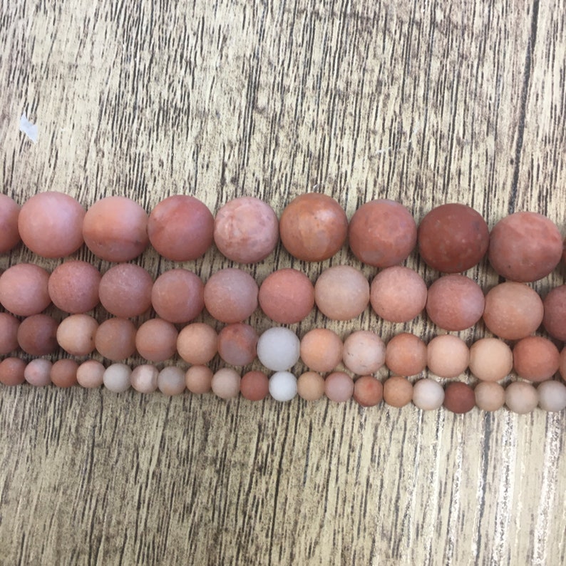 May include: A strand of smooth, round, red agate beads in various sizes. The beads are arranged in rows, with the largest beads at the top and the smallest beads at the bottom.