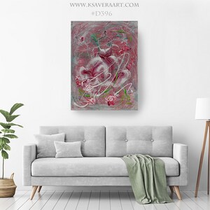 May include: Abstract painting of a pink dress with white and green floral details on a gray background. The painting is framed and hanging on a white wall above a gray couch.