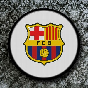 May include: A white and yellow embroidered patch with the FC Barcelona logo. The logo features a red and blue shield with a yellow soccer ball and the letters FCB.