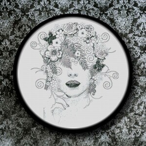 May include: Black and white cross stitch embroidery of a woman's face with flowers and leaves surrounding her head.
