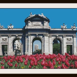 May include: A large stone archway with three arches, a white inscription, and decorative sculptures. The archway is surrounded by a bed of bright pink tulips.