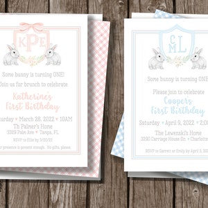 May include: Two pink and blue first birthday party invitations with bunny rabbits and a monogrammed shield. The pink invitation says "Katherine's First Birthday" and the blue invitation says "Cooper's First Birthday".