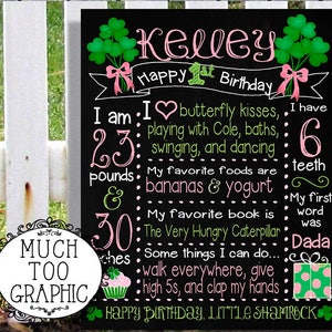 May include: A black chalkboard with a pink and green shamrock theme. It says "Kelley Happy 1st Birthday" and lists facts about the child, including their weight, favourite foods, and first word. The text "Happy Birthday, Little Shamrock" is at the bottom.